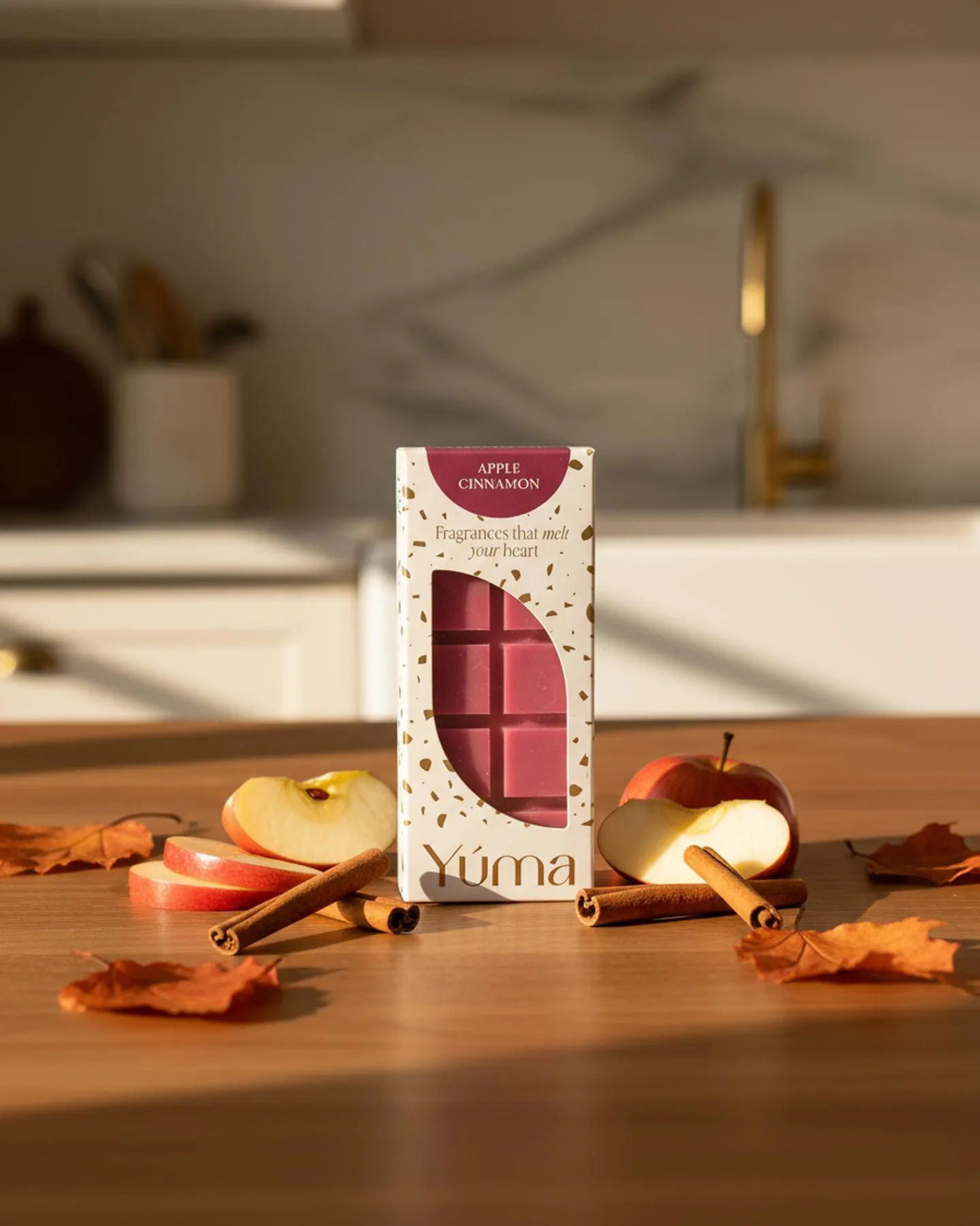 Συσκευασία Apple Cinnamon wax melts της YUMA ανάμεσα σε φέτες μήλου, ξυλάκια κανέλας και φθινοπωρινά φύλλα.