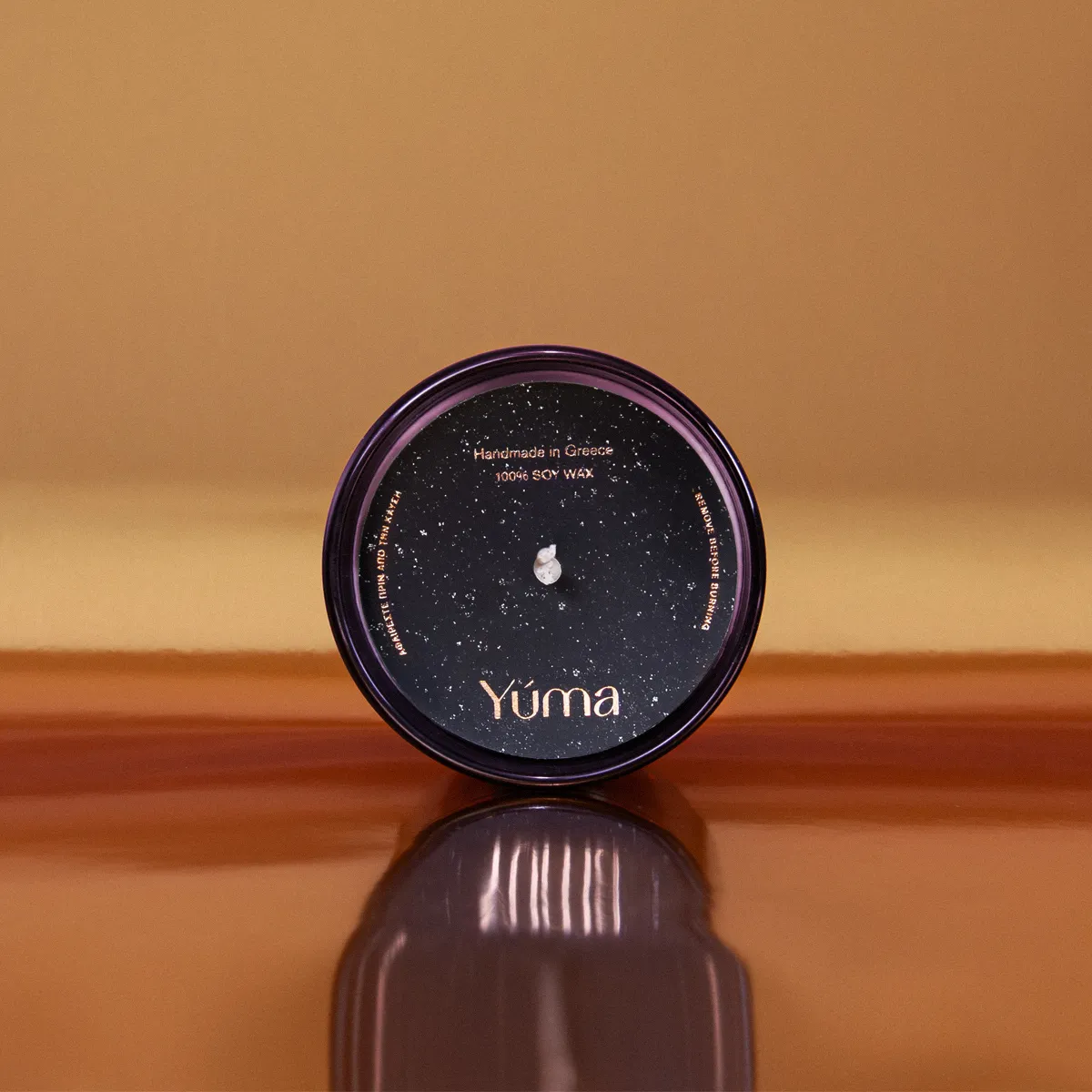 Κερί Apple Cinnamon της YUMA σε καπνιστό ροζ γυάλινο δοχείο με μαύρο κάλυμμα σε καφέ φόντο.