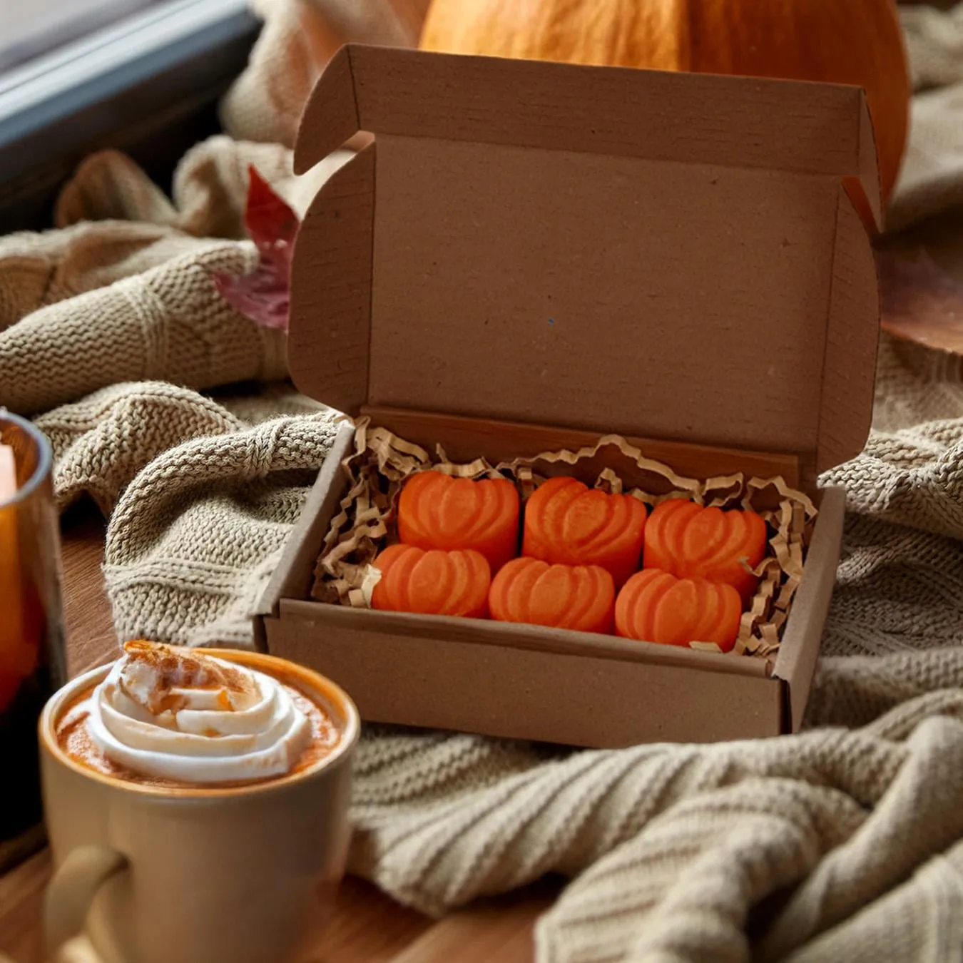 Έξι πορτοκαλί wax melts Pumpkin Pie σε σχήμα κολοκύθας μέσα σε χάρτινο κουτί δίπλα σε ρόφημα.