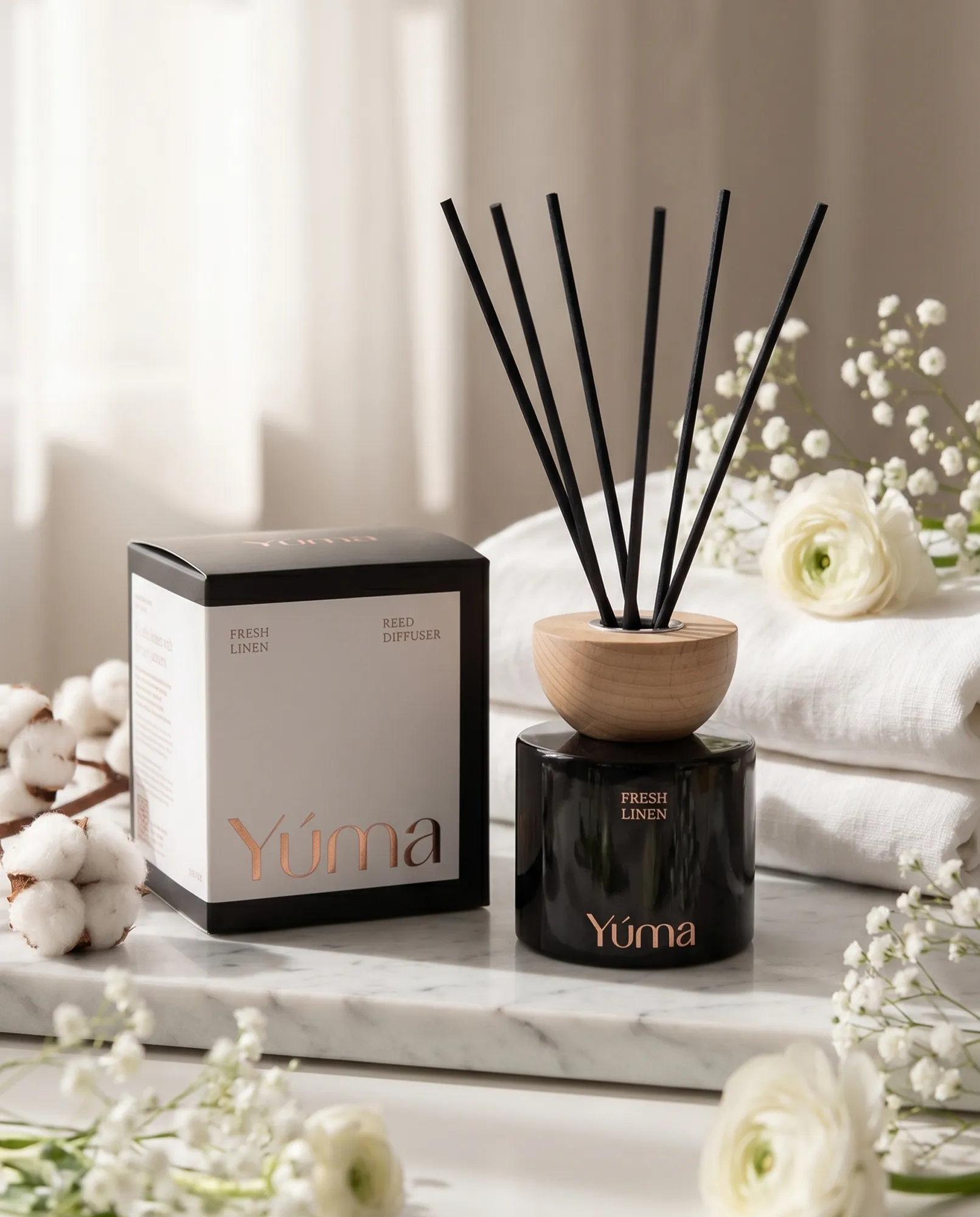 Reed diffuser Fresh Linen της YUMA δίπλα σε λευκές πετσέτες, άνθη βαμβακιού και μικρά λευκά λουλούδια.