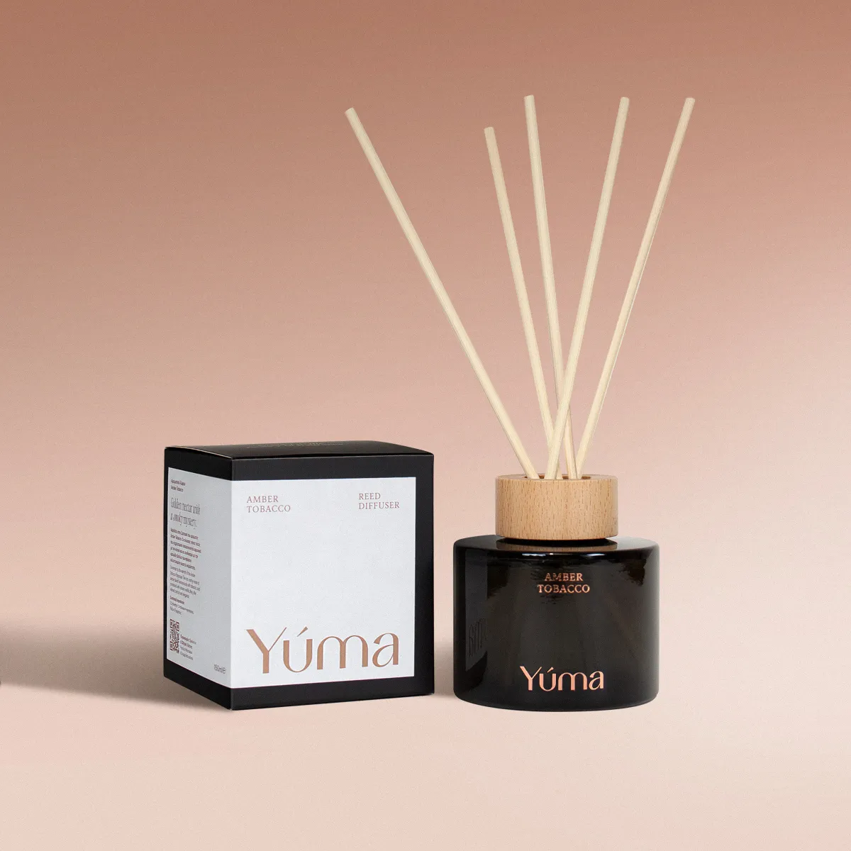 Reed diffuser Amber Tobacco της YUMA σε σκούρο γυάλινο μπουκάλι δίπλα στη χάρτινη συσκευασία του.