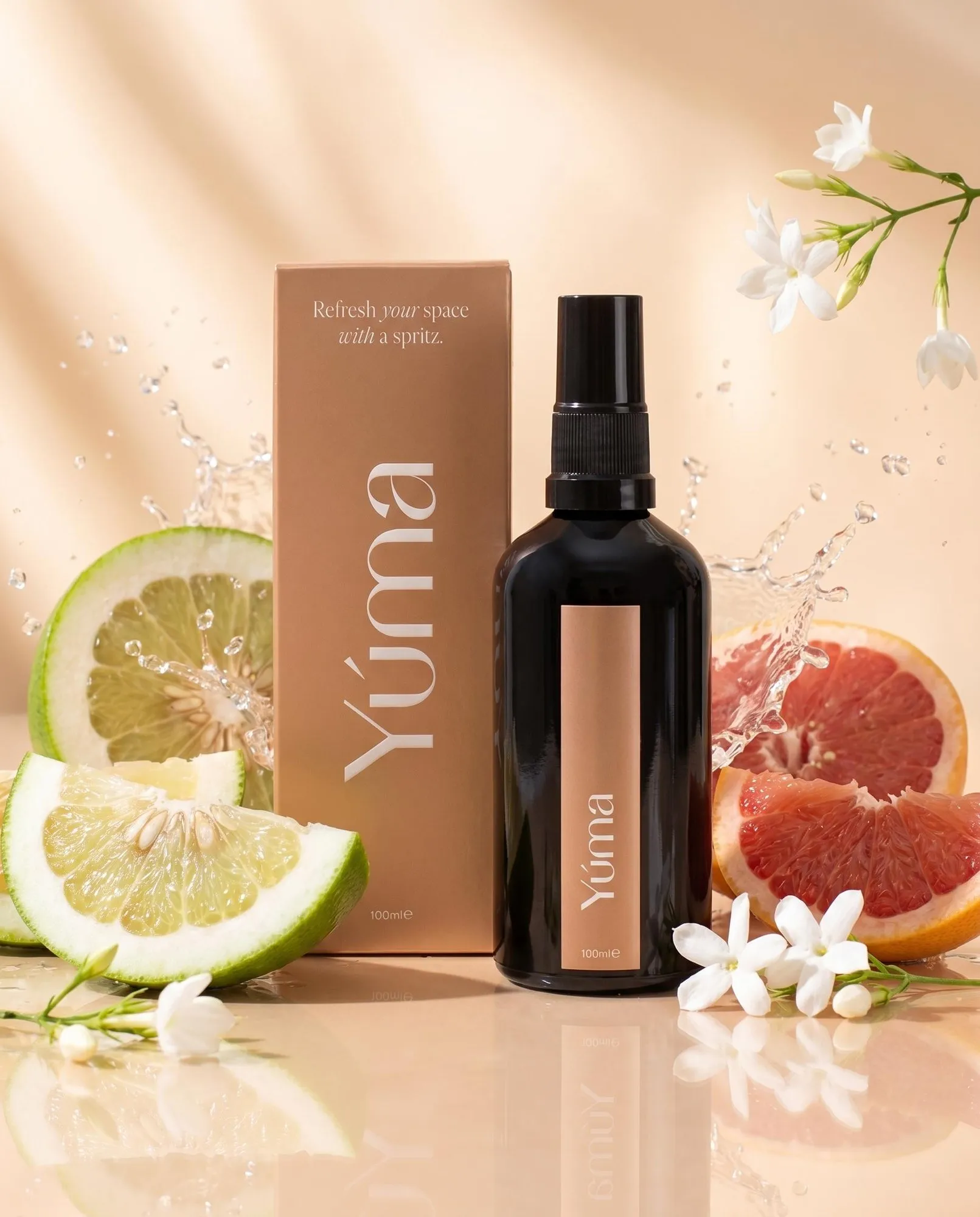 Σκούρο μπουκάλι spray και κουτί YUMA Hesperides Jasmine ανάμεσα σε φέτες εσπεριδοειδών, γιασεμί και σταγόνες νερού.