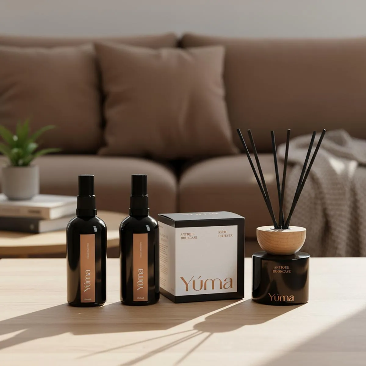 Δύο room sprays, ένα κουτί και ένα Antique Bookcase reed diffuser της YUMA σε ξύλινο τραπέζι.