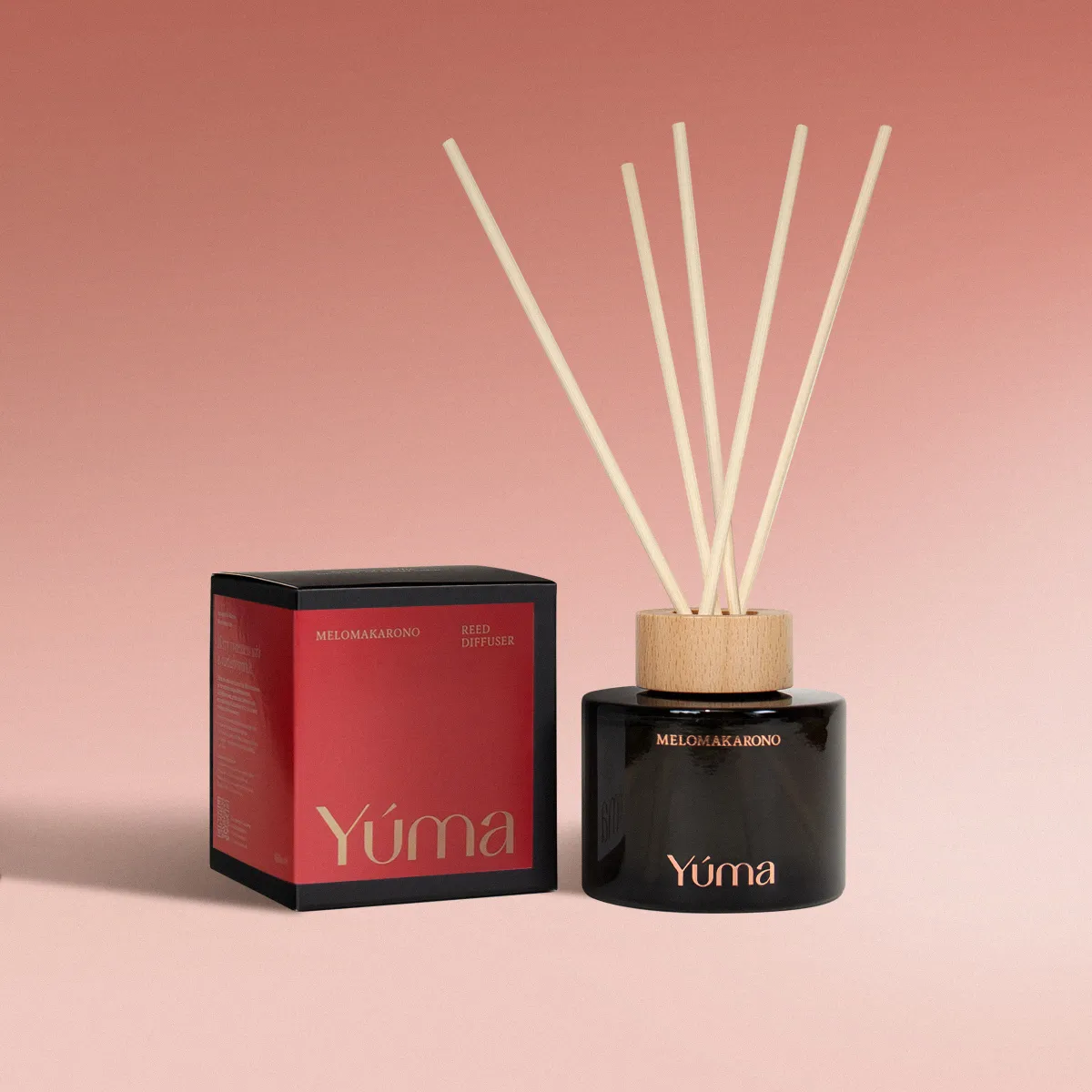 Reed diffuser Melomakarono της YUMA σε μαύρο γυάλινο δοχείο δίπλα στην κόκκινη συσκευασία του.