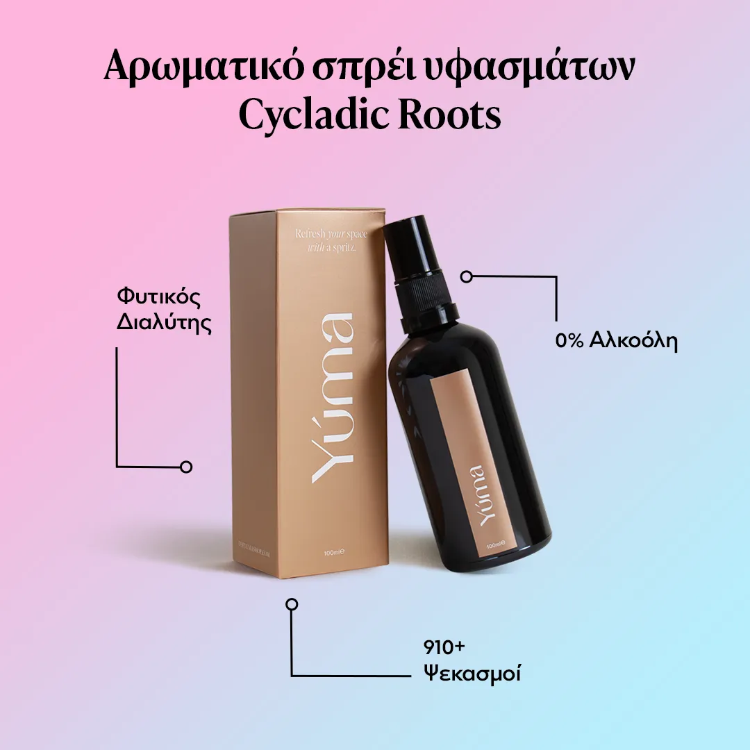 Σκούρο γυάλινο μπουκάλι σπρέι υφασμάτων Cycladic Roots της YUMA δίπλα στη χρυσή συσκευασία του.