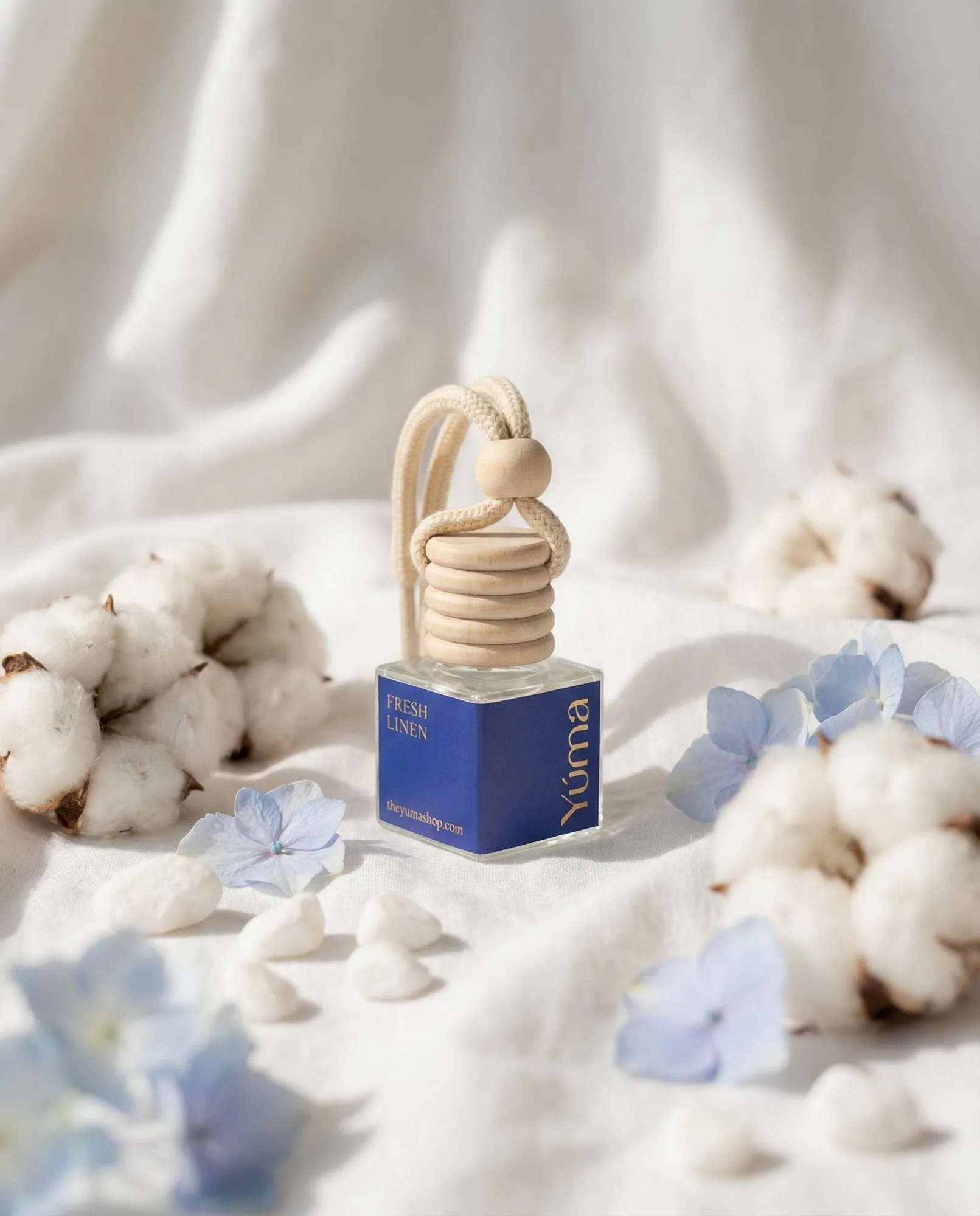 Car Diffuser της YUMA με άρωμα Fresh Linen ανάμεσα σε άνθη βαμβακιού και γαλάζια λουλούδια.