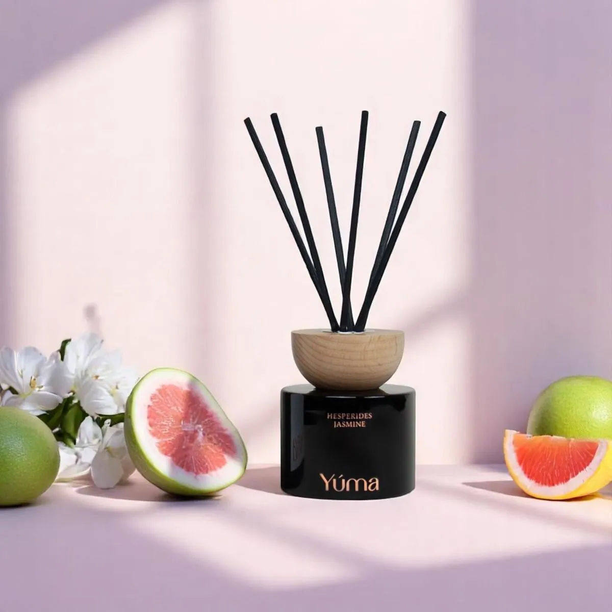 Reed diffuser Hesperides Jasmine της YUMA με μαύρα στικς, πλαισιωμένο από κομμένα γκρέιπφρουτ και λευκά άνθη.