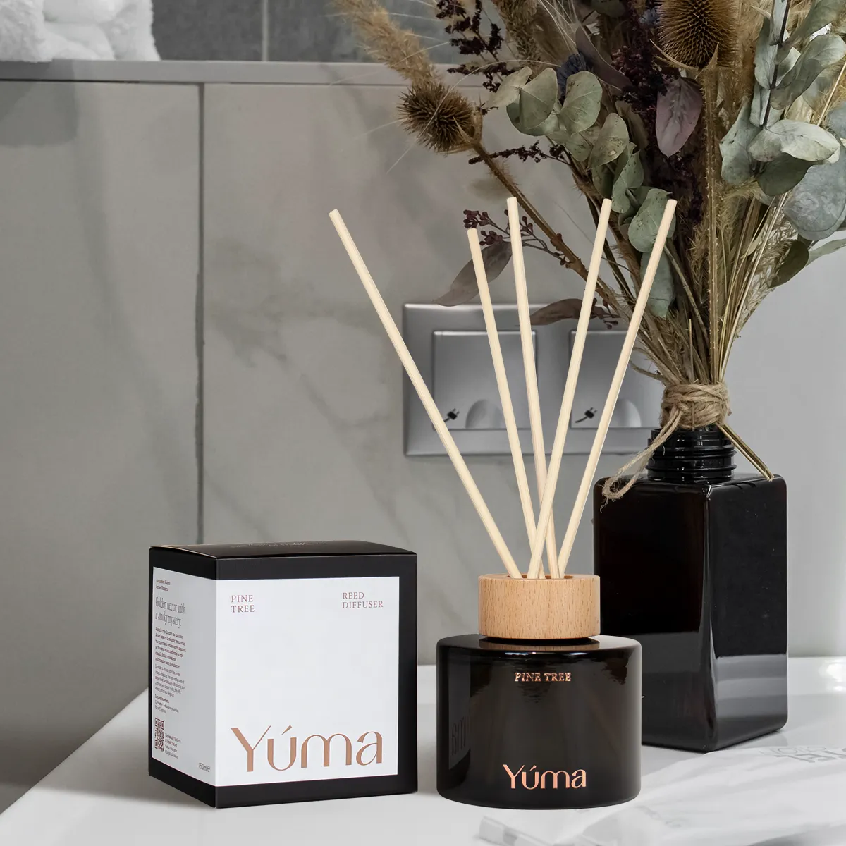 Reed diffuser Pine Tree της YUMA σε σκούρο γυάλινο δοχείο δίπλα στη συσκευασία του.