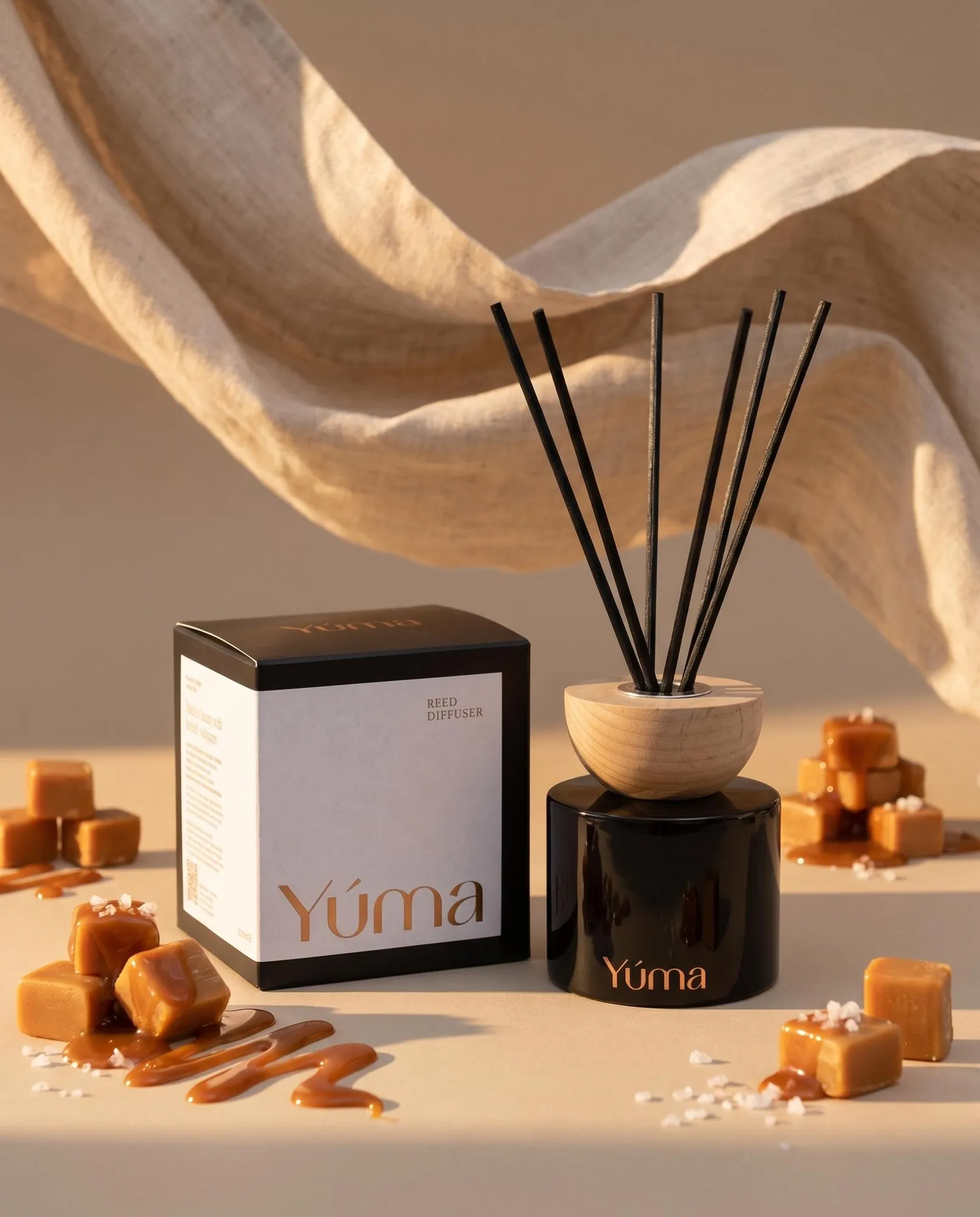 Reed diffuser της YUMA με άρωμα Salted Caramel δίπλα σε κύβους καραμέλας και χοντρό αλάτι.
