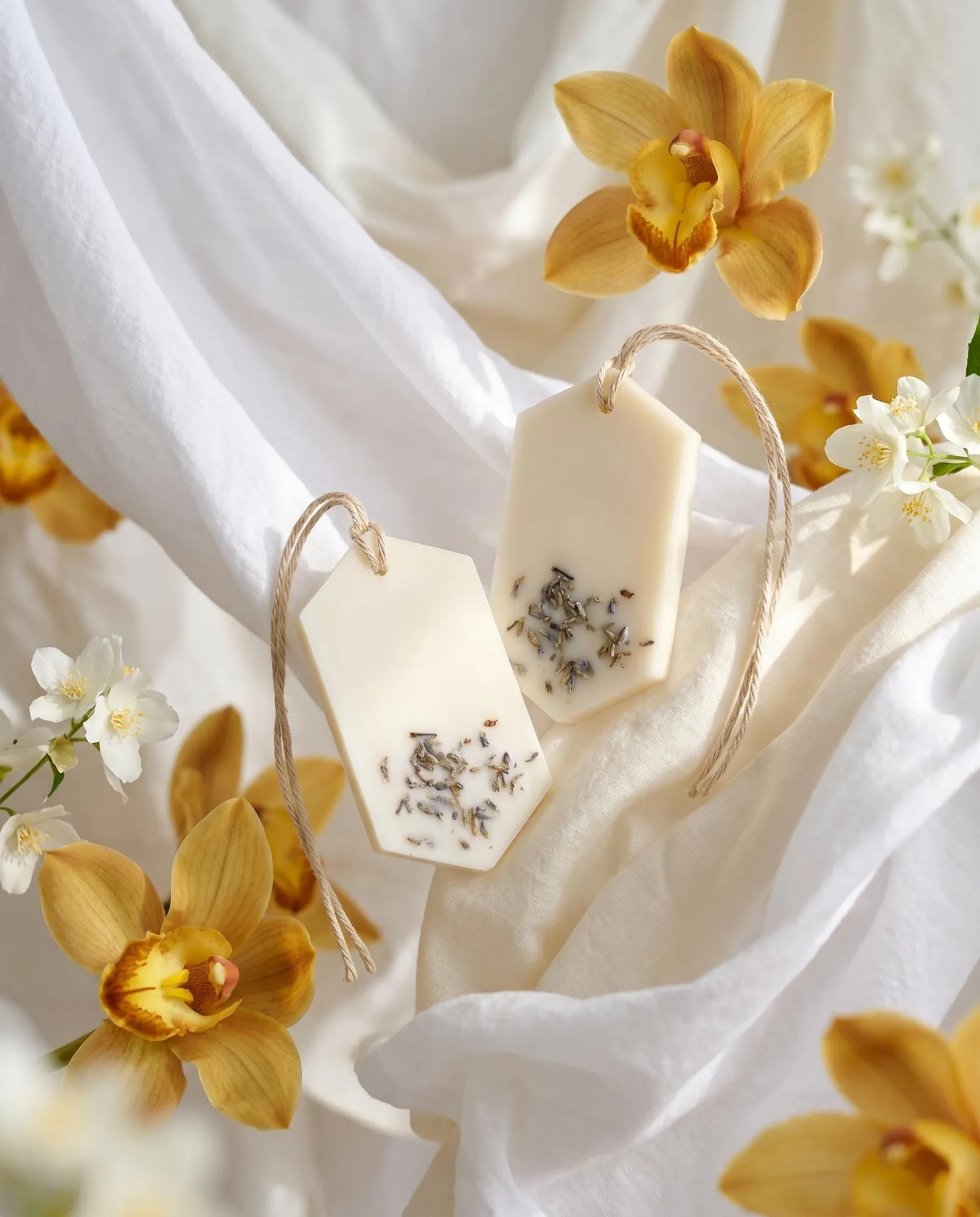 Δύο Gold Orchid Wax Tablets κρεμασμένα ανάμεσα σε λευκά υφάσματα και κίτρινες ορχιδέες.