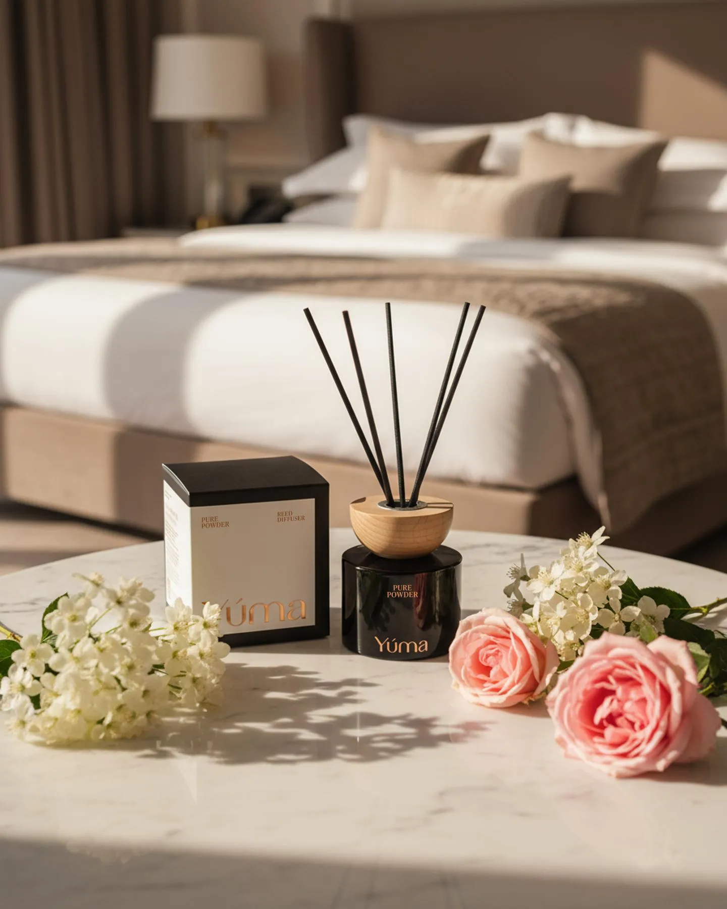 Reed diffuser Pure Powder της YUMA με μαύρα στικς δίπλα σε ροζ τριαντάφυλλα πάνω σε μαρμάρινο τραπέζι.