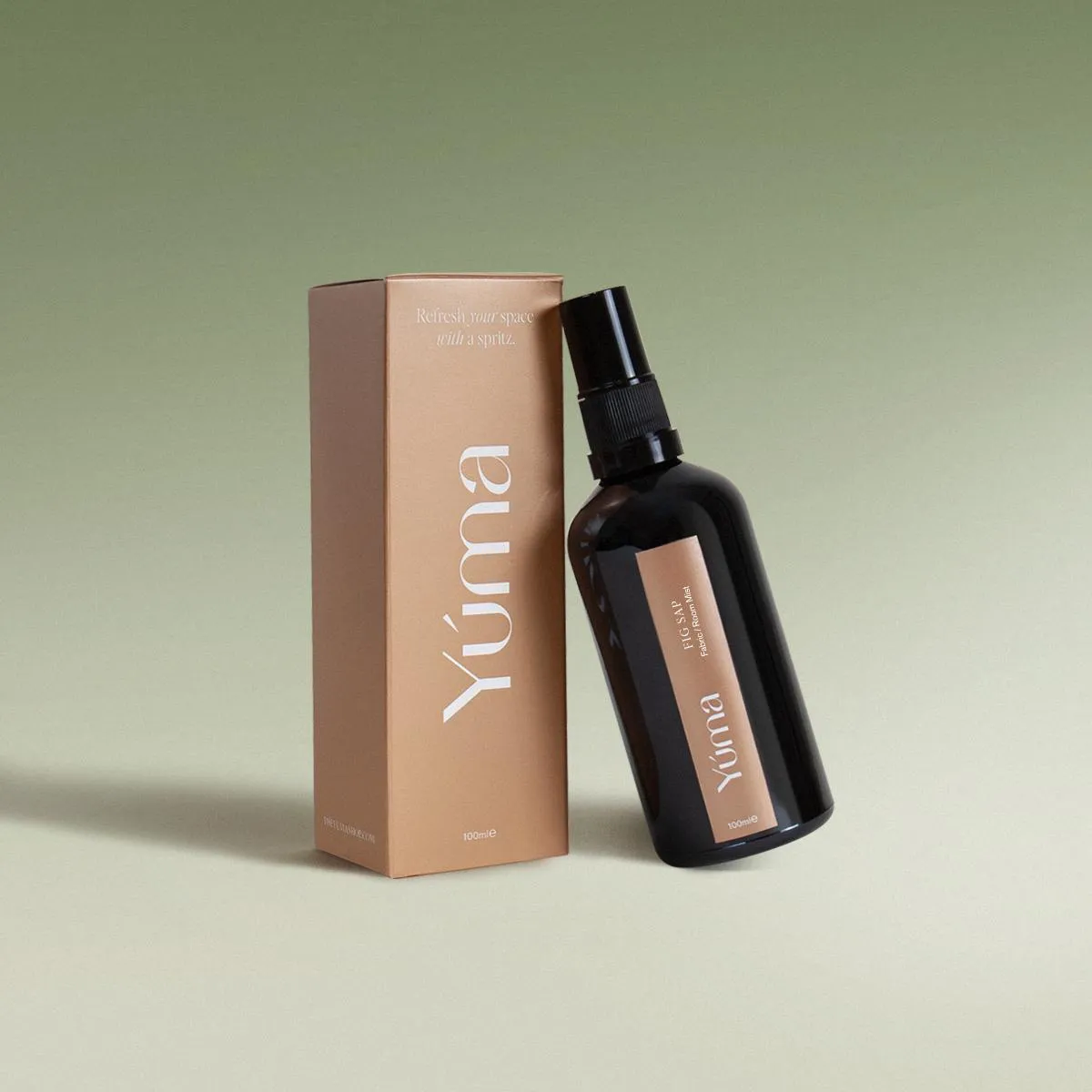 Σκούρο γυάλινο μπουκάλι Fabric Mist Fig Sap της YUMA δίπλα στην καφέ χάρτινη συσκευασία του.