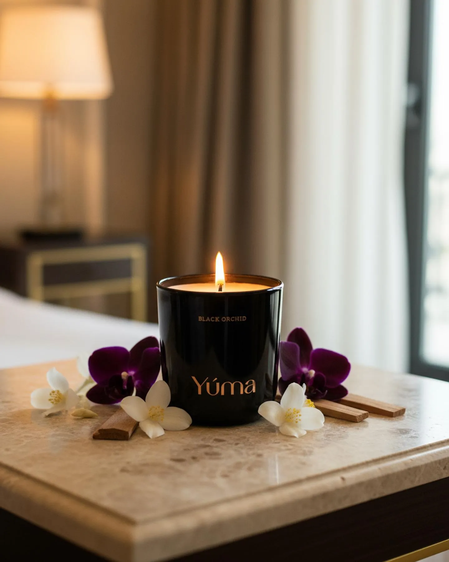 Αναμμένο κερί Black Orchid της YUMA σε μαύρο γυάλινο δοχείο ανάμεσα σε μωβ ορχιδέες και λευκά άνθη.