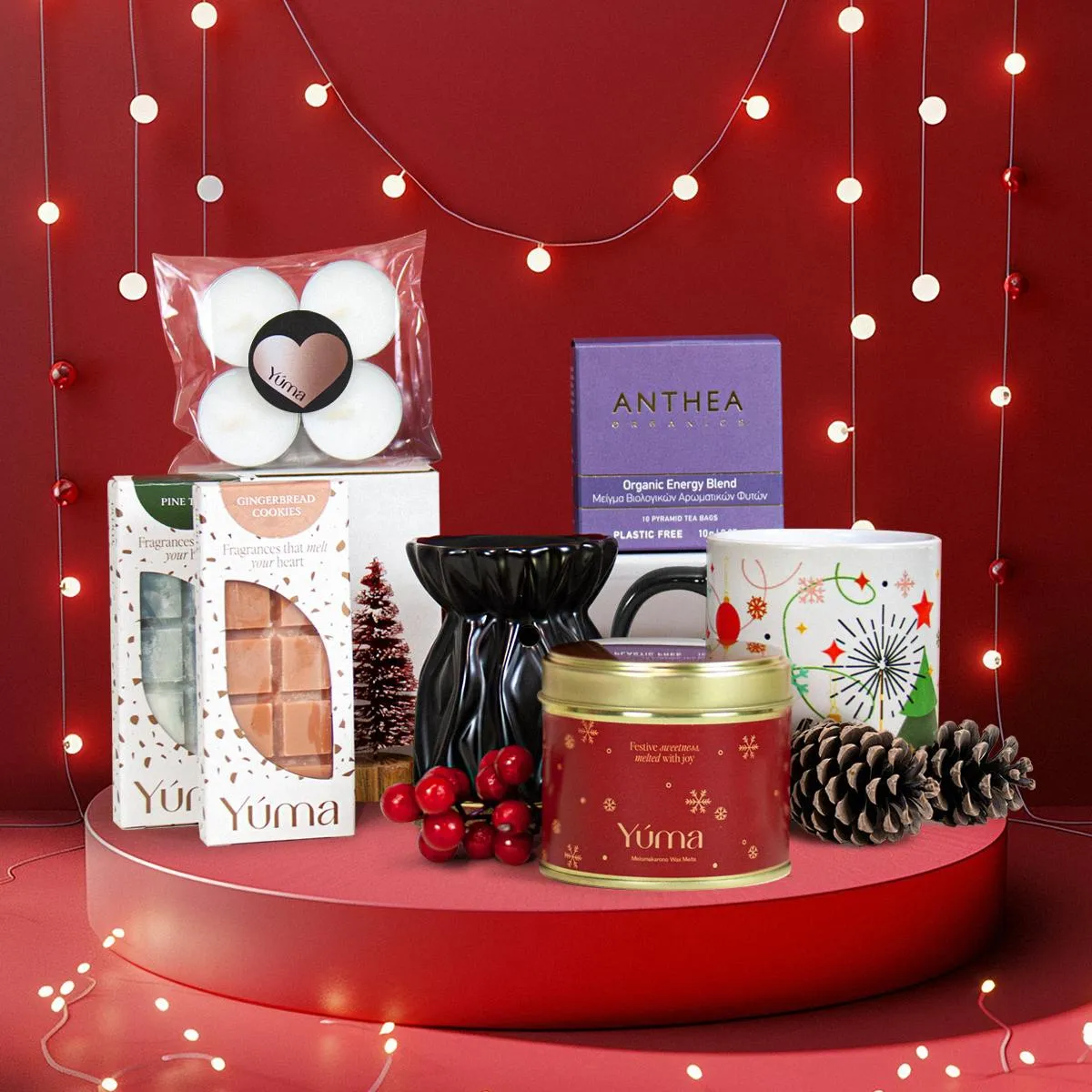 Χριστουγεννιάτικο Gift Set της YUMA με wax melts, αρωματικό κερί, κούπα και διακοσμητικά κουκουνάρια σε κόκκινο φόντο.
