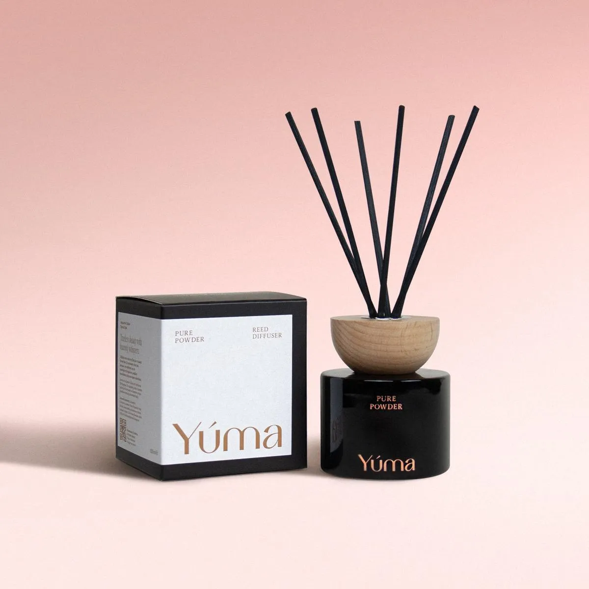 Pure Powder Reed Diffuser Reed diffuser Pure Powder της YUMA σε μαύρο γυάλινο δοχείο δίπλα στη χάρτινη συσκευασία του.