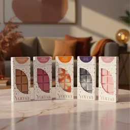 Signature Collection - Wax Melt Set Πέντε χρωματιστά wax melts της YUMA σε λευκές συσκευασίες πάνω σε μαρμάρινο τραπέζι σαλονιού.
