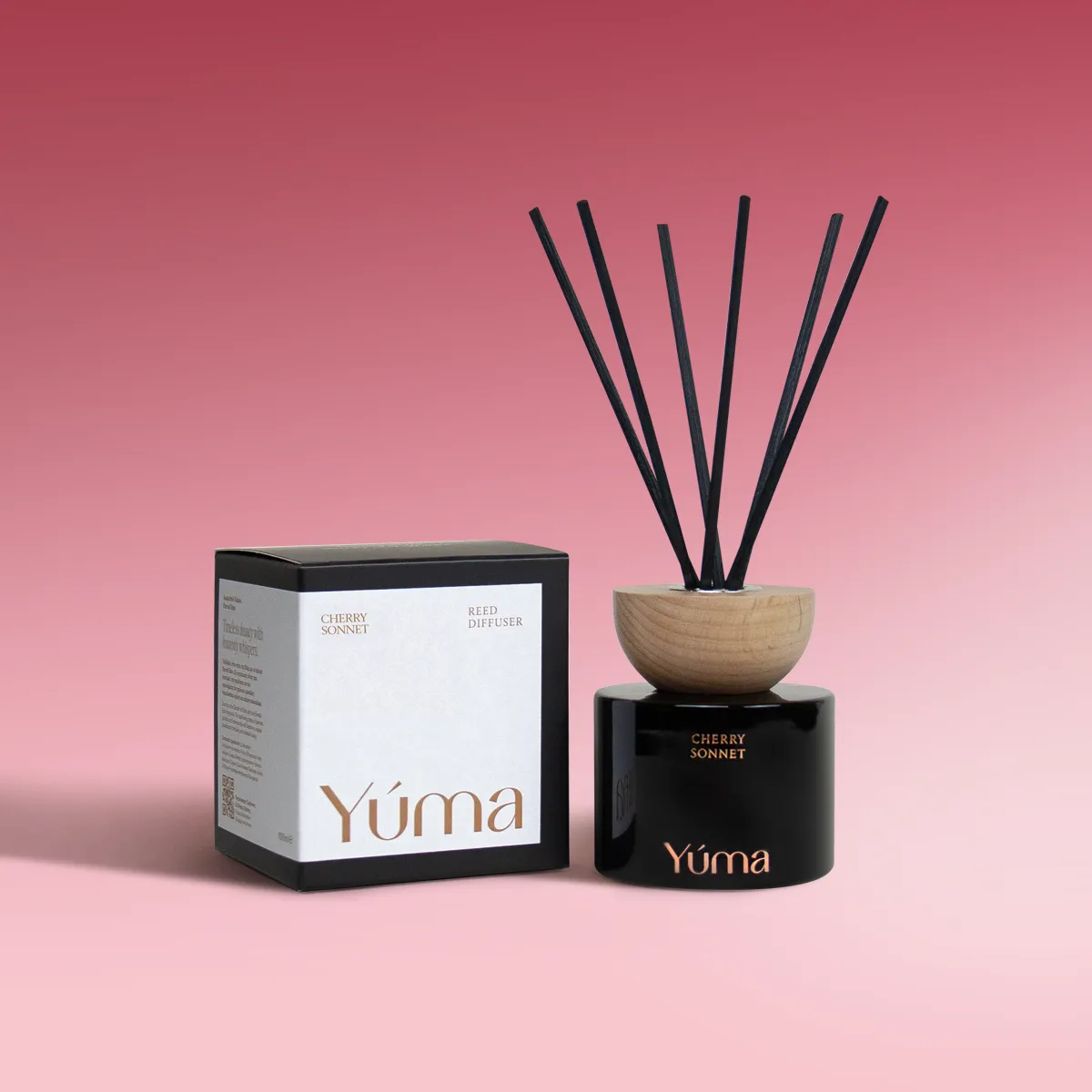 Cherry Sonnet Reed Diffuser Μαύρο γυάλινο reed diffuser Cherry Sonnet της YUMA με ξύλινο πώμα και το κουτί του σε ροζ φόντο.