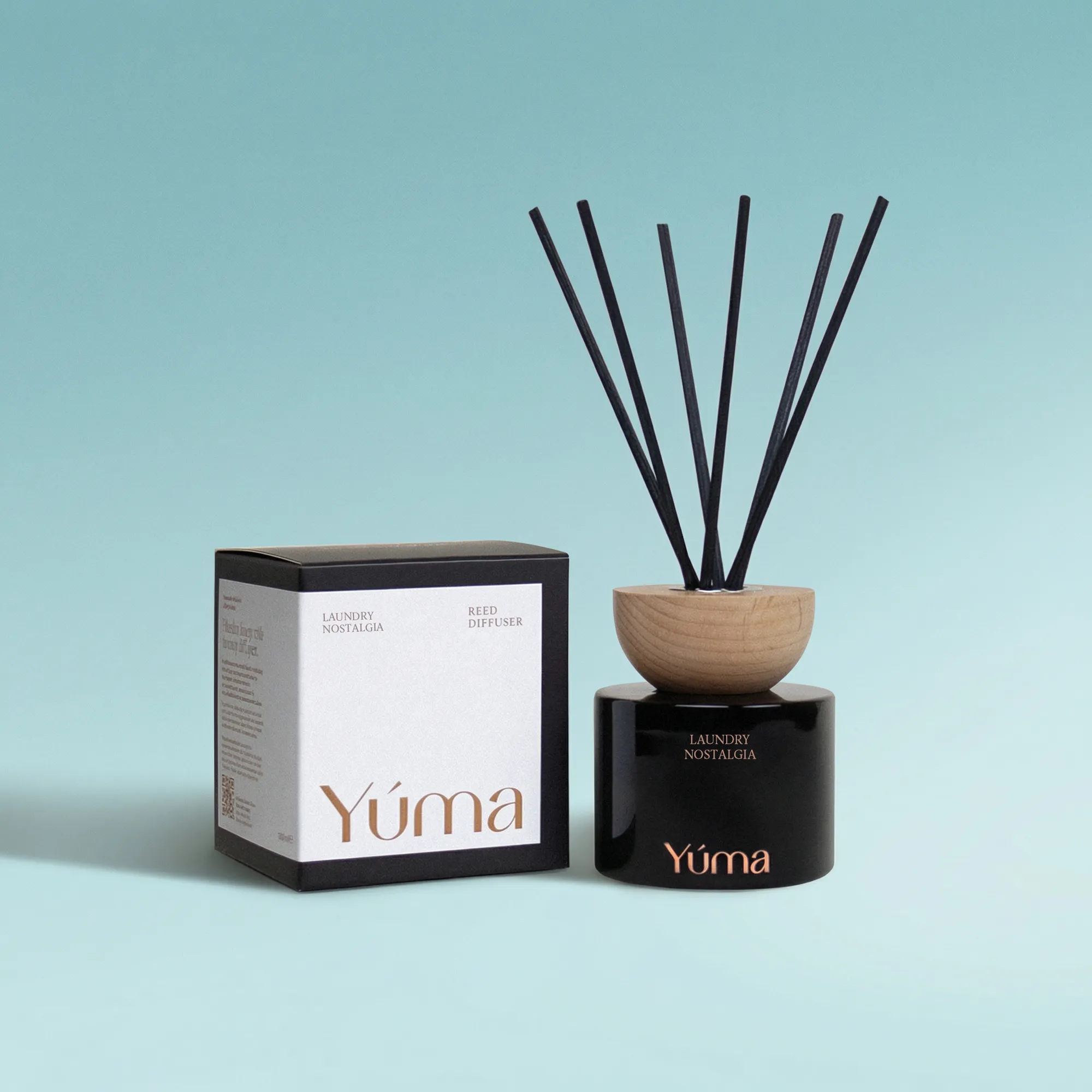 Laundry Nostalgia Reed Diffuser Reed diffuser Laundry Nostalgia της YUMA σε μαύρο γυάλινο δοχείο δίπλα στη χάρτινη συσκευασία του.