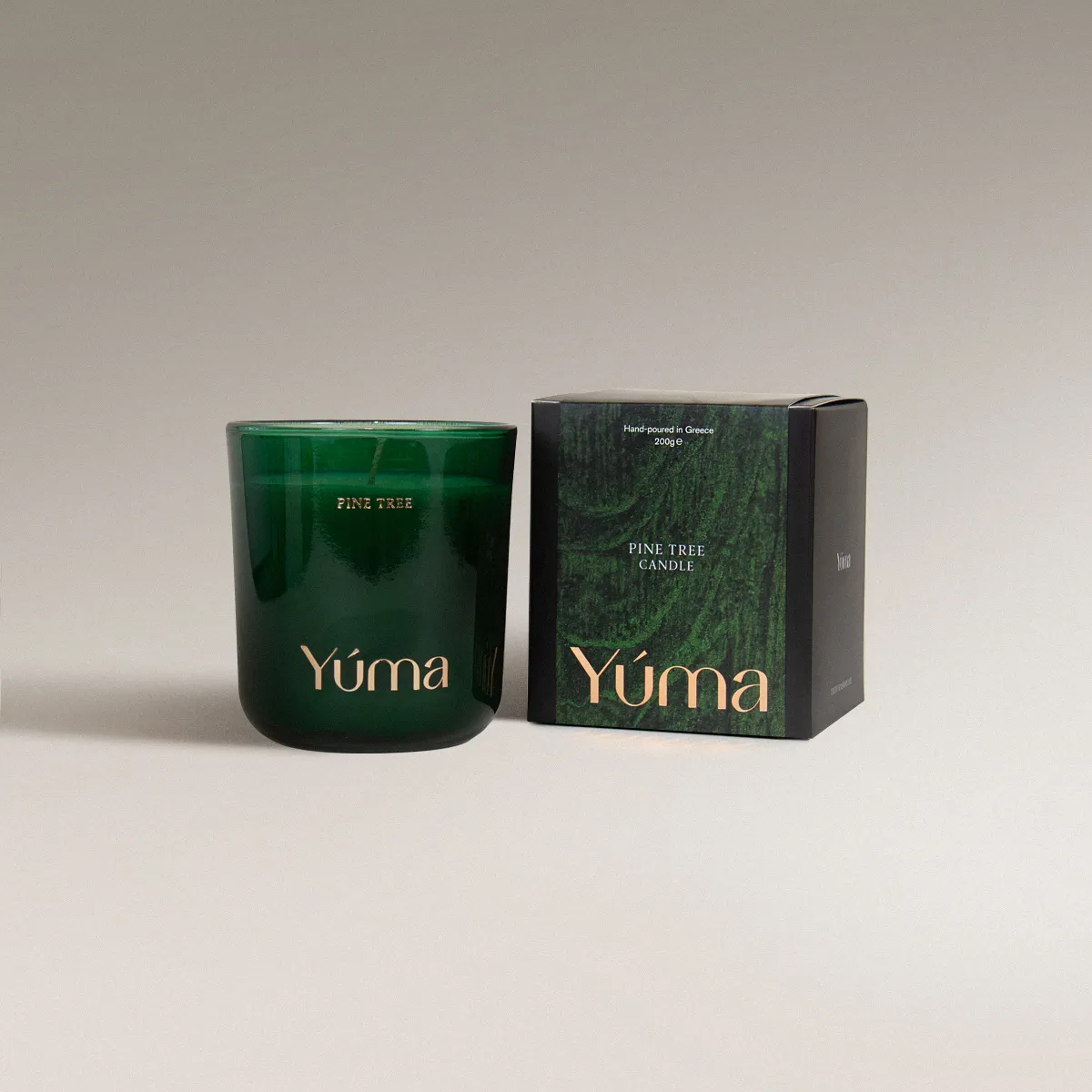 Pine Tree Candle Πράσινο γυάλινο κερί Pine Tree της YUMA δίπλα στη χάρτινη συσκευασία του σε γκρι φόντο.