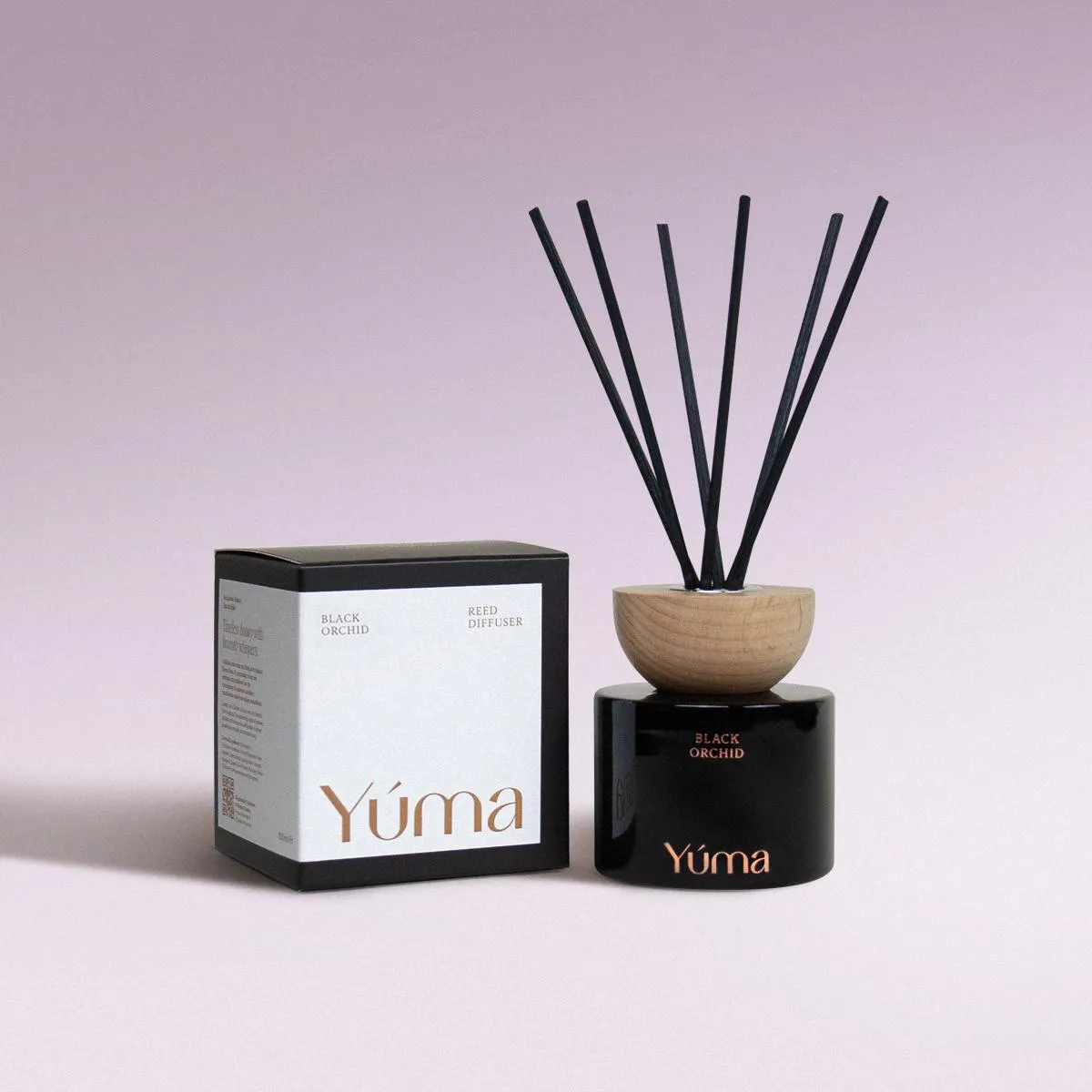 Black Orchid Reed Diffuser Reed diffuser Black Orchid της YUMA σε μαύρο γυάλινο δοχείο δίπλα στη χάρτινη συσκευασία του.