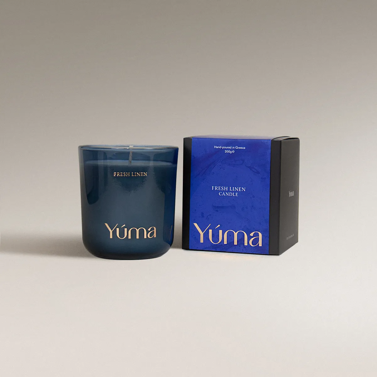 Fresh Linen Candle Μπλε γυάλινο κερί Fresh Linen της YUMA δίπλα στη χάρτινη συσκευασία του.