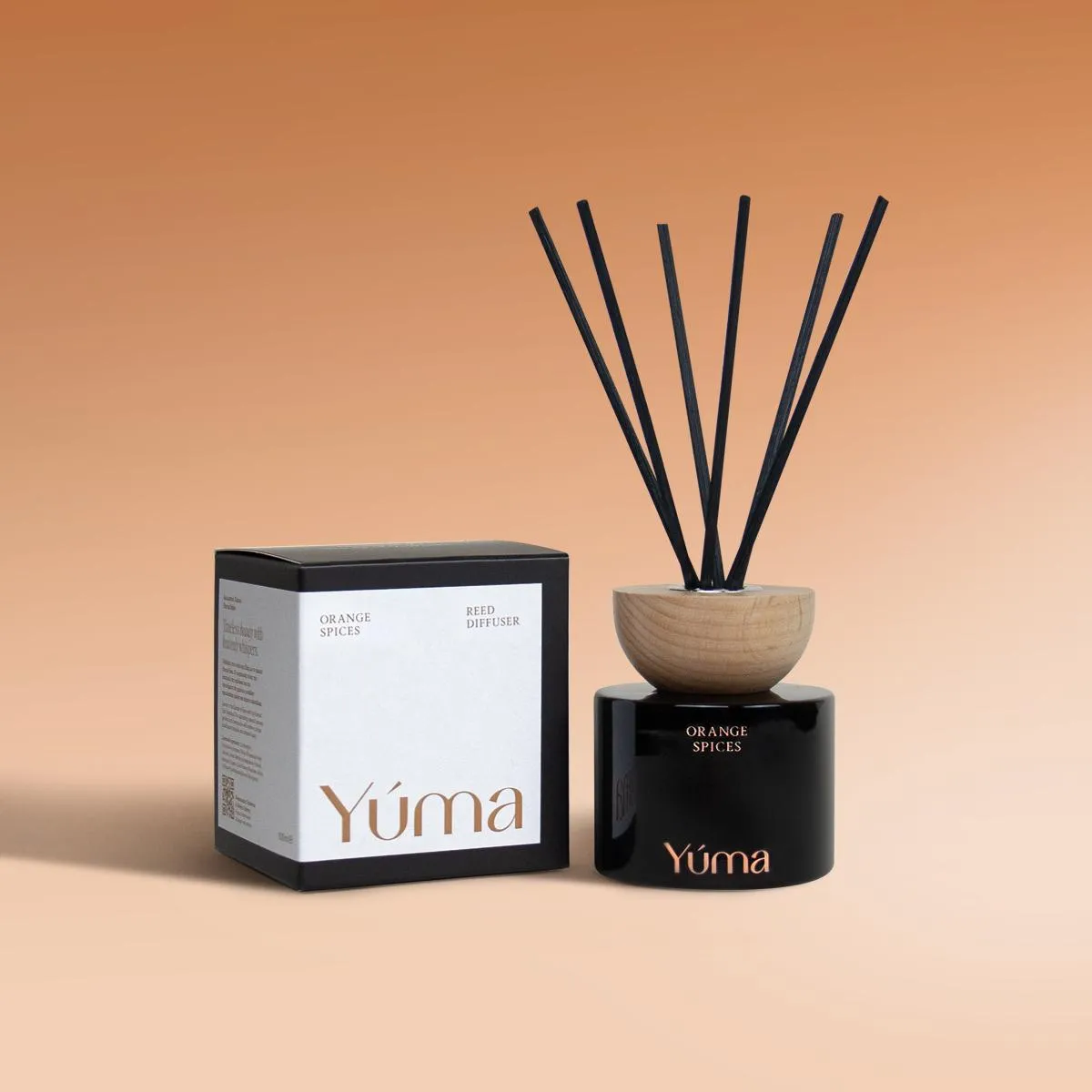 Orange Spices Reed Diffuser Reed diffuser Orange Spices της YUMA σε μαύρο γυάλινο δοχείο δίπλα στη συσκευασία του.