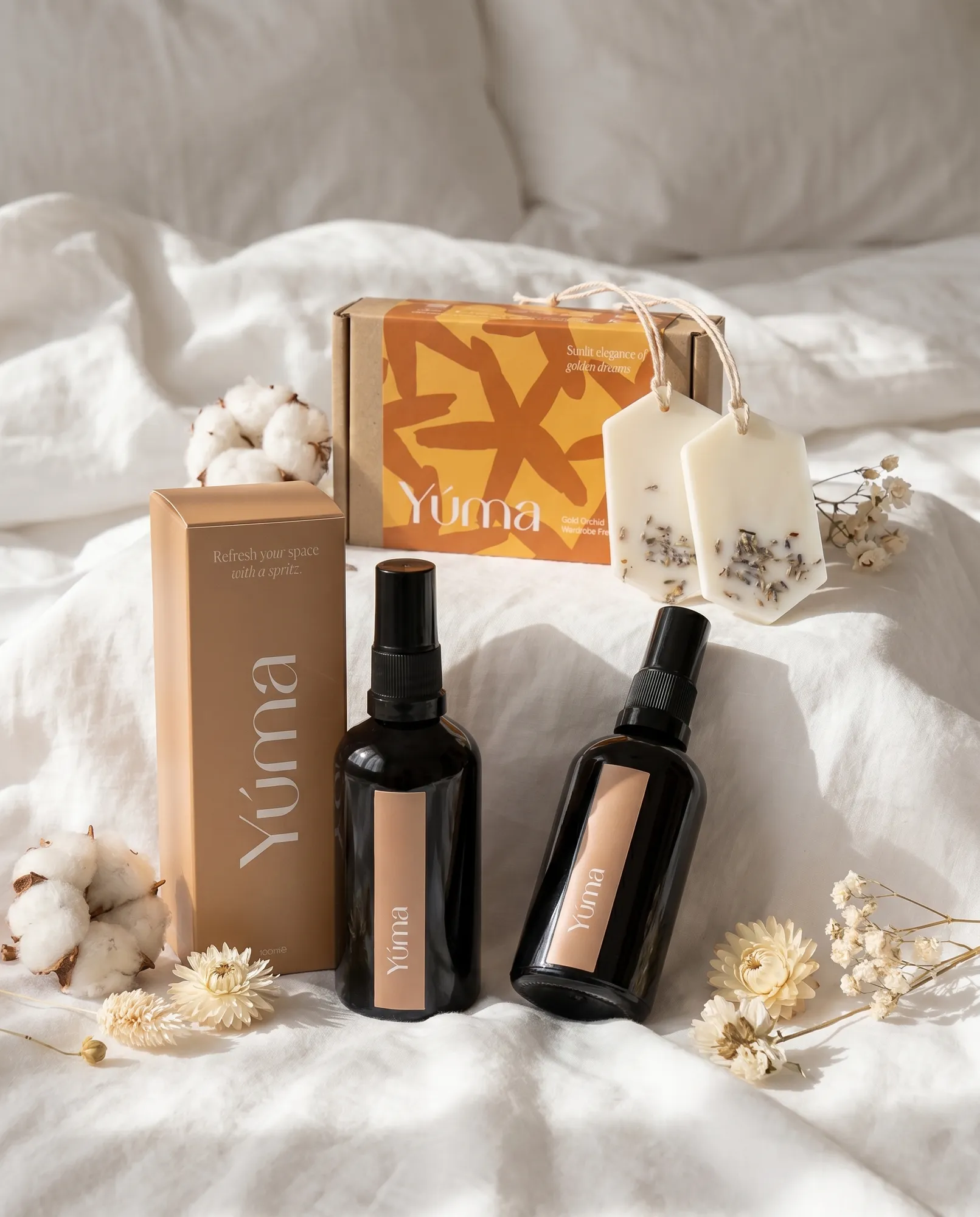 Linen Set Fresh Linen και Pure Powder Fabric/Room Mist με Gold Orchid Wax Tablets και κουτί YUMA πάνω σε λευκά σεντόνια.