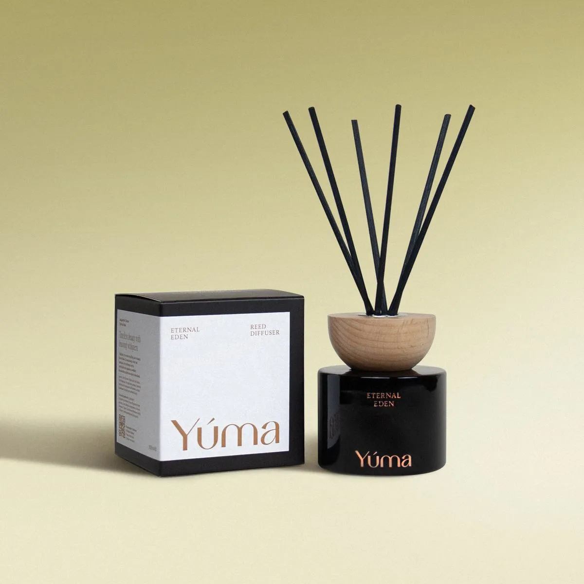 Eternal Eden Reed Diffuser Reed diffuser Eternal Eden της YUMA σε μαύρο γυάλινο δοχείο δίπλα στη χάρτινη συσκευασία του.