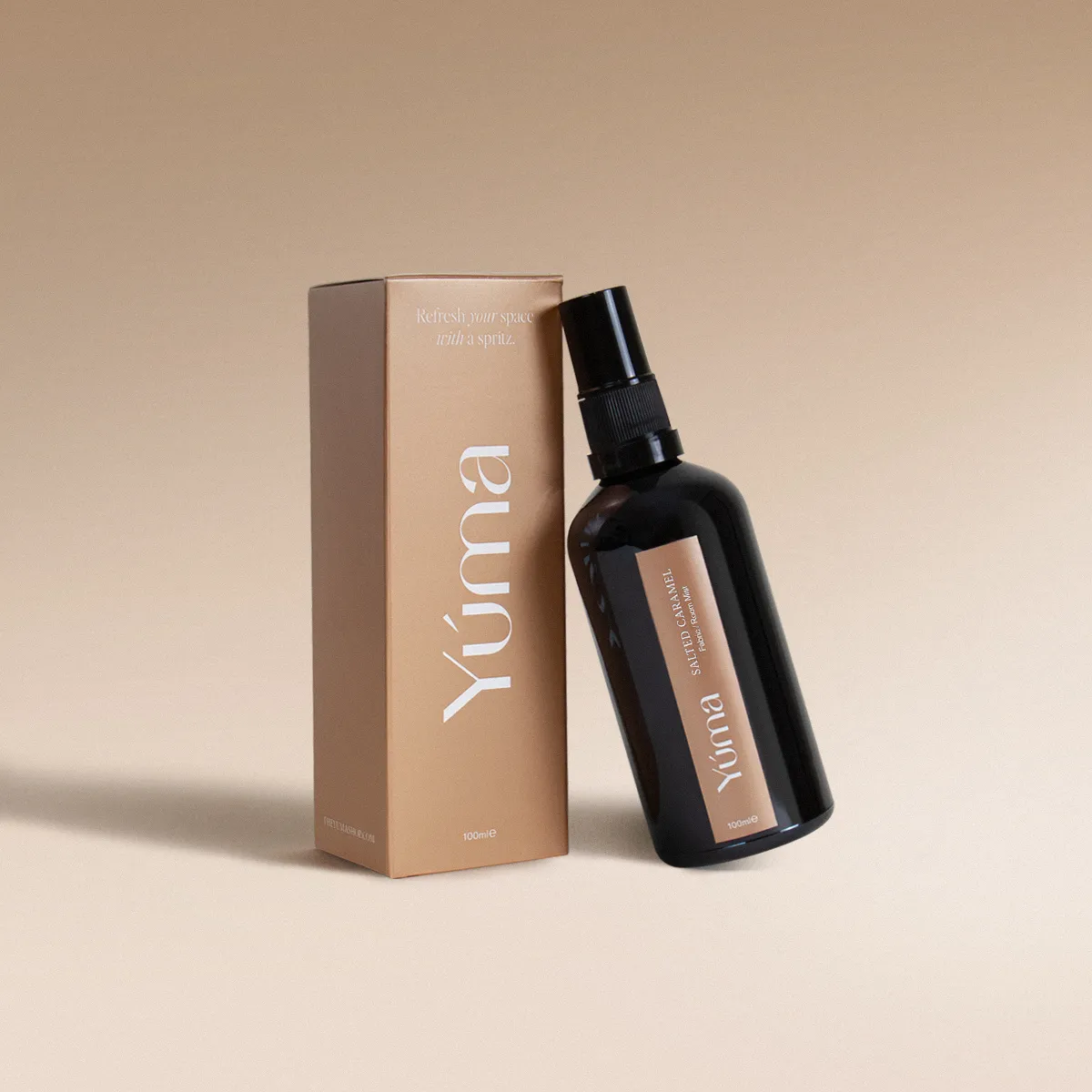 Salted Caramel Fabric/Room Mist Σκούρο γυάλινο μπουκάλι Fabric Mist Salted Caramel της YUMA δίπλα στην μπεζ χάρτινη συσκευασία του.