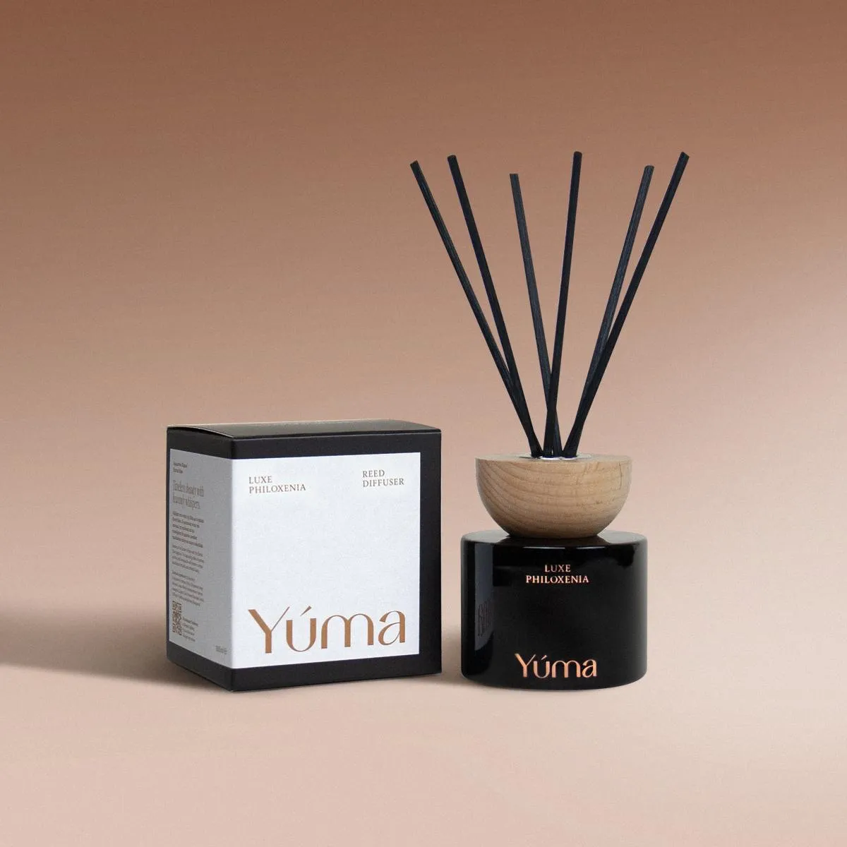 Luxe Philoxenia Reed Diffuser Reed diffuser Luxe Philoxenia της YUMA σε μαύρο γυάλινο δοχείο δίπλα στη συσκευασία του.